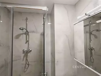 Moderní koupelna s elegantními dlaždicemi, sprchovým koutem a skleněnými dveřmi. Světlé povrchy vytvářejí prostorný a čistý vzhled.