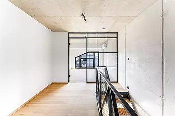 Průmyslová chodba s parketovou podlahou, industriálním zábradlím a velkými okny, moderní design s betonovými stropy.