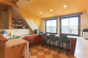 Podkrovní kuchyň s dlažbou, moderní linkou a vestavěnými spotřebiči. Velká okna poskytují výhled a přirozené světlo.