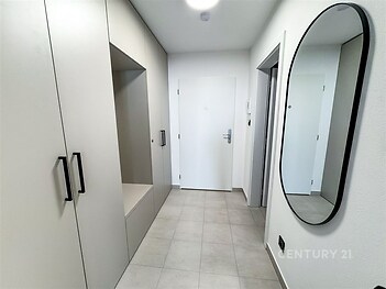 Úzká předsíň s dlažbou a vestavěnými skříněmi. Moderní interiér s velkým zrcadlem na stěně, bílé dveře a světlé barvy.