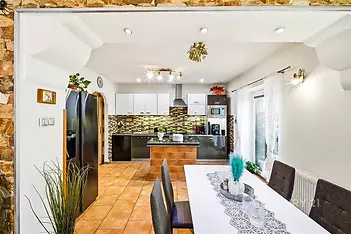 Moderní kuchyň s dlažbou, vestavěné spotřebiče a světlé dekorace, prostorný jídelní kout s bílým stolem a elegantními židlemi.