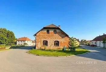 Zrekonstruovaný cihlový dům s šikmou střechou a moderní fasádou se nachází na klidné ulici s asfaltovou příjezdovou cestou a zeleným okolím.
