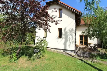Zahrada s rodinným domem, dřevěná terasa, moderní architektura, stromy pro soukromí, světlá fasáda, zelený trávník, klidná lokalita.