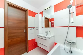 Koupelna s moderními dlaždicemi, bílou sanitou a vanou. Stylové dřevěné dveře a světlý interiér zajišťují elegantní vzhled.