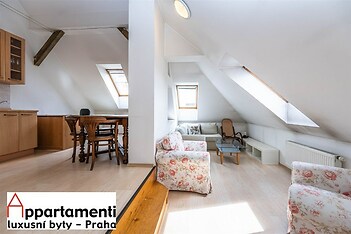 Světlý podkrovní obývací pokoj, světlá parketová podlaha, velká střešní okna, moderní interiér s dřevěným nábytkem, rekonstruovaný prostor.