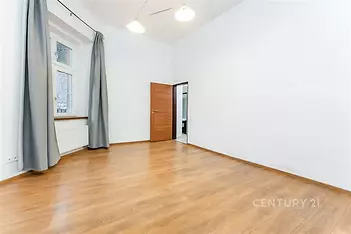 Světlý pokoj s parketovou podlahou a velkými okny, stylový moderní design, bílé stěny a dřevěné dveře nabízejí prostorné a vzdušné prostředí.