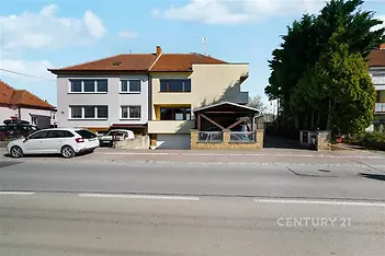 Exteriér rodinného domu s parkovacími místy, šikmou střechou a upravenou zahradou v klidné ulici. Fasáda v moderním stylu.