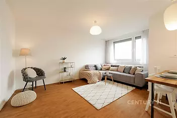 Světlý obývací pokoj s parketovou podlahou, velká okna, moderní nábytek a minimalistický design dodávají místnosti vzdušnost a pohodlí.