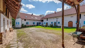 Dvůr s historickými zemědělskými budovami, kamenná dlažba, staré dřevěné vrata, rekonstrukce původního stylu.