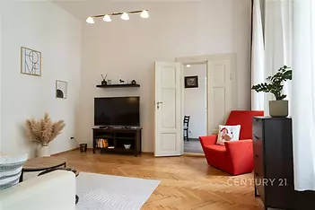 Světlý obývací pokoj s parketovou podlahou, velkými okny a moderním nábytkem, nabízí útulné prostředí pro relaxaci.