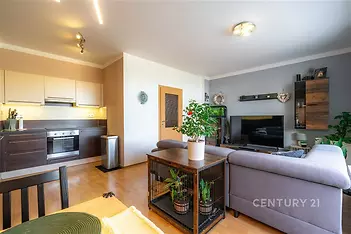 Světlý obývací pokoj s parketovou podlahou, otevřený k moderní kuchyni, vybavený velkými okny a vkusným nábytkem, ideální pro pohodlné bydlení.