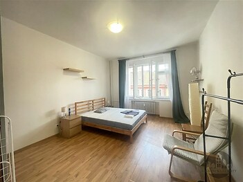 Světlá ložnice s parketovou podlahou, velká okna, moderní nábytek a minimalistický styl.
