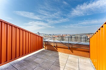Střešní terasa s dlažbou, moderní zábradlí a výhled na město. Světlé prostředí a prostorný design ideální pro relaxaci nebo večírky.