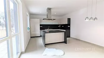 Moderní kuchyň s dlažbou, velká okna zajišťující světlost, elegantní černobílá linka s centrálním ostrůvkem, závěsná svítidla přidávají styl.