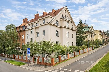 Rohový bytový dům s kachlovou střechou a zahradou, nachází se v klidné čtvrti, bloková architektura s renovovanou fasádou.