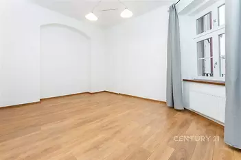 Světlý obývací pokoj s parketovou podlahou a velkými okny, moderní výzdoba a vysoké stropy vytvářejí prostorný dojem.
