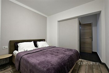 Prostorná ložnice s dřevěnou podlahou, moderní design a přírodní tóny, vybavená pohodlnou postelí a velkými polštáři.