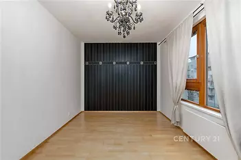Prázdná místnost s parketovou podlahou, velkým oknem a moderním lustrem. Vhodná pro světlý a stylový interiér.