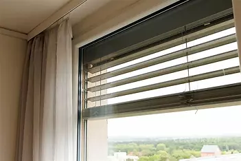 Velké okno s moderními žaluziemi nabízí úchvatný výhled. Světlý interiér s elegantními závěsy a důrazem na přirozené osvětlení.