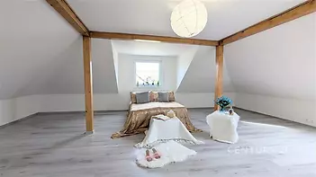 Podkrovní ložnice s moderními dřevěnými trámy, světlou parketovou podlahou a velkým oknem poskytujícím dostatek přirozeného světla.