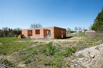 Nedokončená stavba na otevřené ploše s cihlovými zdmi a betonovou základovou deskou, ideální pro rekonstrukci na rodinný dům