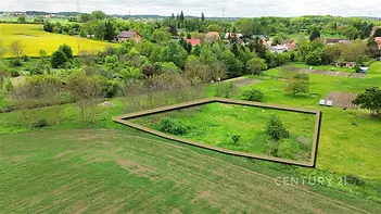 Pohled na stavební pozemek obklopený zelení, rovinatý terén, klidná lokalita, v blízkosti vesnické zástavby, ideální pro rodinný dům.