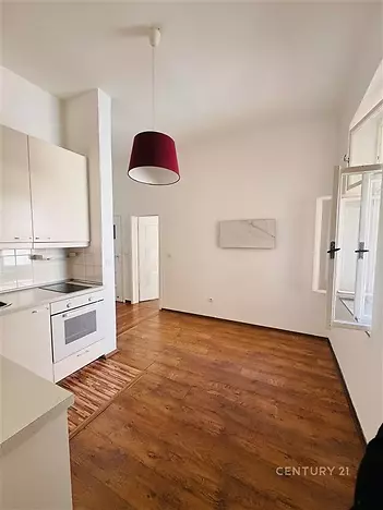 Kuchyňský kout s dřevěnou podlahou, světlými skříňkami a velkým oknem, moderní spotřebiče zajišťují pohodlí a útulnost.