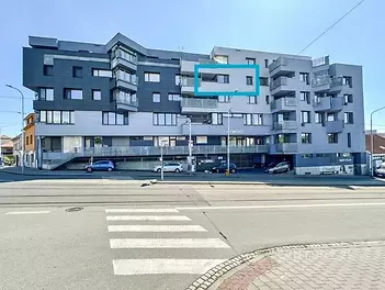 Moderní bytový dům s balkonem, fasáda v šedých tónech, velká okna, výborný stav budovy, nachází se v klidné městské lokalitě.
