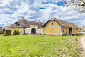 Historický exteriér venkovského stavení s žlutou fasádou, šikmou střechou a rozsáhlým travnatým pozemkem, vhodný pro rekonstrukci.