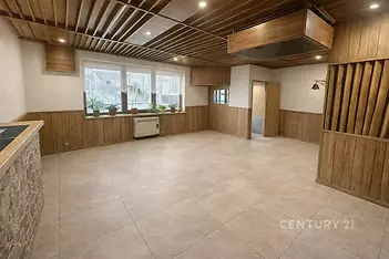 Světlý obývací pokoj s dlažbou, dřevěným obložením a velkými okny, nabízí moderní design a prostorný interiér.