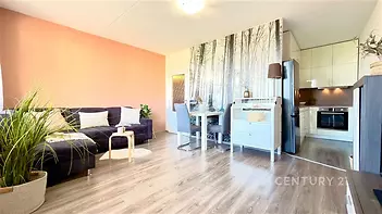 Světlý obývací pokoj s parketovou podlahou, moderní kuchyň s vestavěnými spotřebiči a dekorativní tapetou, vkusně zařízený prostor.