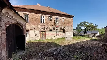 Velký venkovský dům s cihlovou fasádou a šikmou střechou, vyžadující rekonstrukci, obklopený rozlehlým pozemkem.