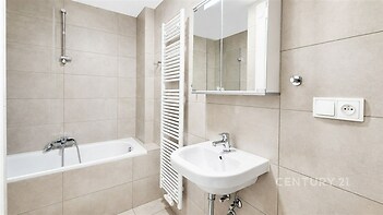 Koupelna s keramickou dlažbou, moderní umyvadlo, vana a nástěnný zrcadlový skříň, světlé neutrální tóny, topný žebřík.