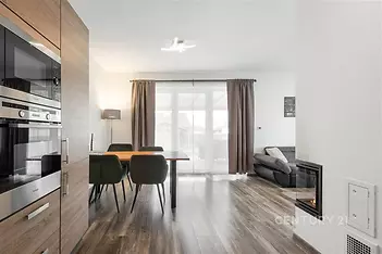 Moderní obývací pokoj s kuchyní, parketová podlaha, velká okna, světlý interiér s vestavěnými spotřebiči a elegantním nábytkem.