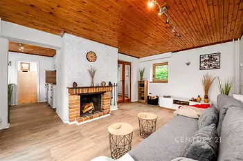 Útulný obývací pokoj s krbovými kamny, dřevěným stropem a parketovou podlahou. Světlý interiér nabízí moderní styl a pohodlí.