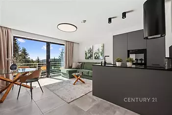 Moderní obývací pokoj s dlažbou, velkými okny a elegantní kuchyní. Světlý prostor s výhledem a moderním designem.