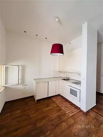 Světlá kuchyň s dřevěnou podlahou, moderními bílými skříňkami a stylovým červeným osvětlením, ideální pro útulné bydlení