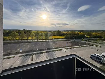 Výhled z balkonu s moderním zábradlím nabízí panoramatický pohled na krajinu a parkoviště, ideální pro milovníky přírody a klidného bydlení.