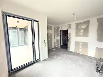 Prázdný pokoj s velkými okny, betonová podlaha, připraven k rekonstrukci, moderní dispozice, světlý interiér, vhodný pro úpravy.