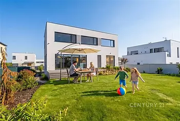 Moderní zahrada s terasou, velká okna, udržovaný trávník, kvalitní dřevěný nábytek, prostorné a světlé venkovní prostředí.