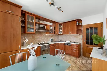 Kuchyň s dřevěnou linkou, dlažba a vestavěné spotřebiče, moderní design, světlý prostor díky velkým oknům.