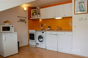 Malá kuchyň s dřevěnou podlahou, vestavěnými spotřebiči a světlými skříňkami, kontrastní oranžová dlažba na zdi, moderní vybavení.