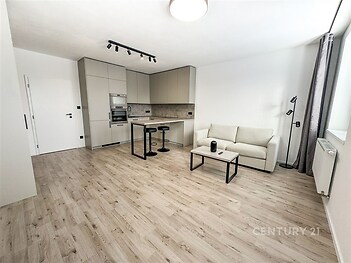 Obývací pokoj s moderní kuchyní, parketová podlaha, světlý interiér, vestavěné spotřebiče, minimalistický styl.