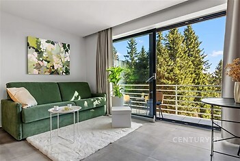 Světlý obývací pokoj s velkými okny, moderní dlažba a zelenou sedačkou, výhled na balkon.