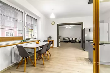 Moderní kuchyň s parketovou podlahou, světlým nábytkem a velkými okny propojená s obývacím pokojem, ideální pro rodinné bydlení.