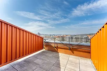 Střešní terasa s dlažbou, moderní zábradlí a výhled na město. Světlé prostředí a prostorný design ideální pro relaxaci nebo večírky.