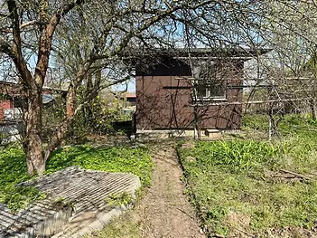 Malá zahradní chatka s dřevěnou fasádou uprostřed klidné zahrady. Okolní zelené stromy poskytují přirozený stín a soukromí.