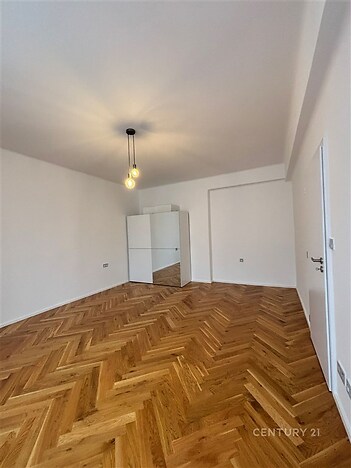 Světlá ložnice s parketovou podlahou a moderním osvětlením, nabízí vestavěné skříně a minimalistický design ve světlých odstínech.