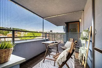 Zastřešený balkon s dřevěným nábytkem, moderní dlažbou a výhledem na město, ideální místo k relaxaci.