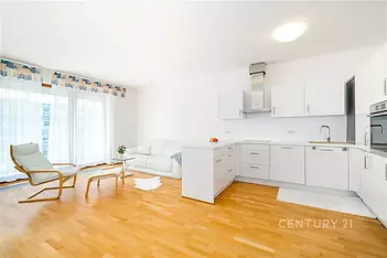 Světlý obývací pokoj s moderní kuchyní, parketová podlaha, velká okna, renovovaný interiér, bílý nábytek, otevřený prostor.